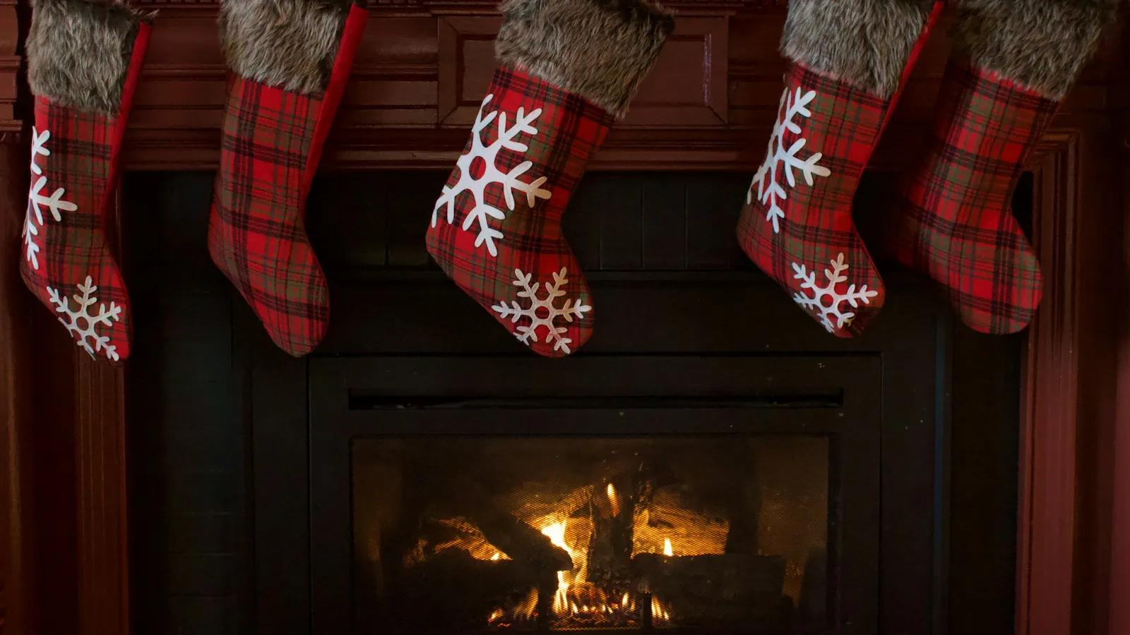 Red plaid and snowflake Christmas stockings hanging above a glowing fireplace