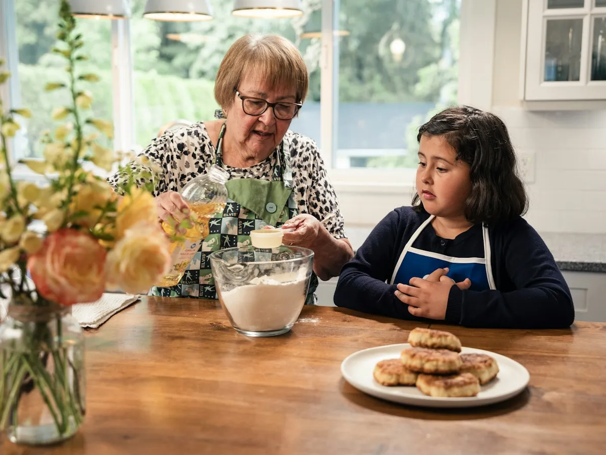 A grandmother and her granddaughter mixing cookie dough together at a kitchen table