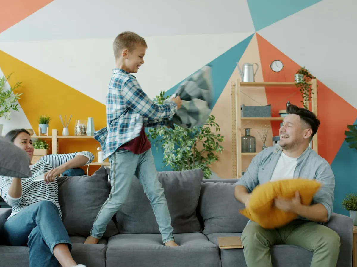 Parents and a boy having a playful pillow fight in a bright living room