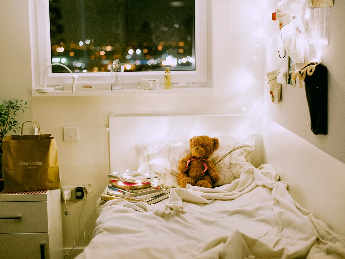 A cozy child’s bedroom at night with fairy lights, a teddy bear on the bed and a warm glow
