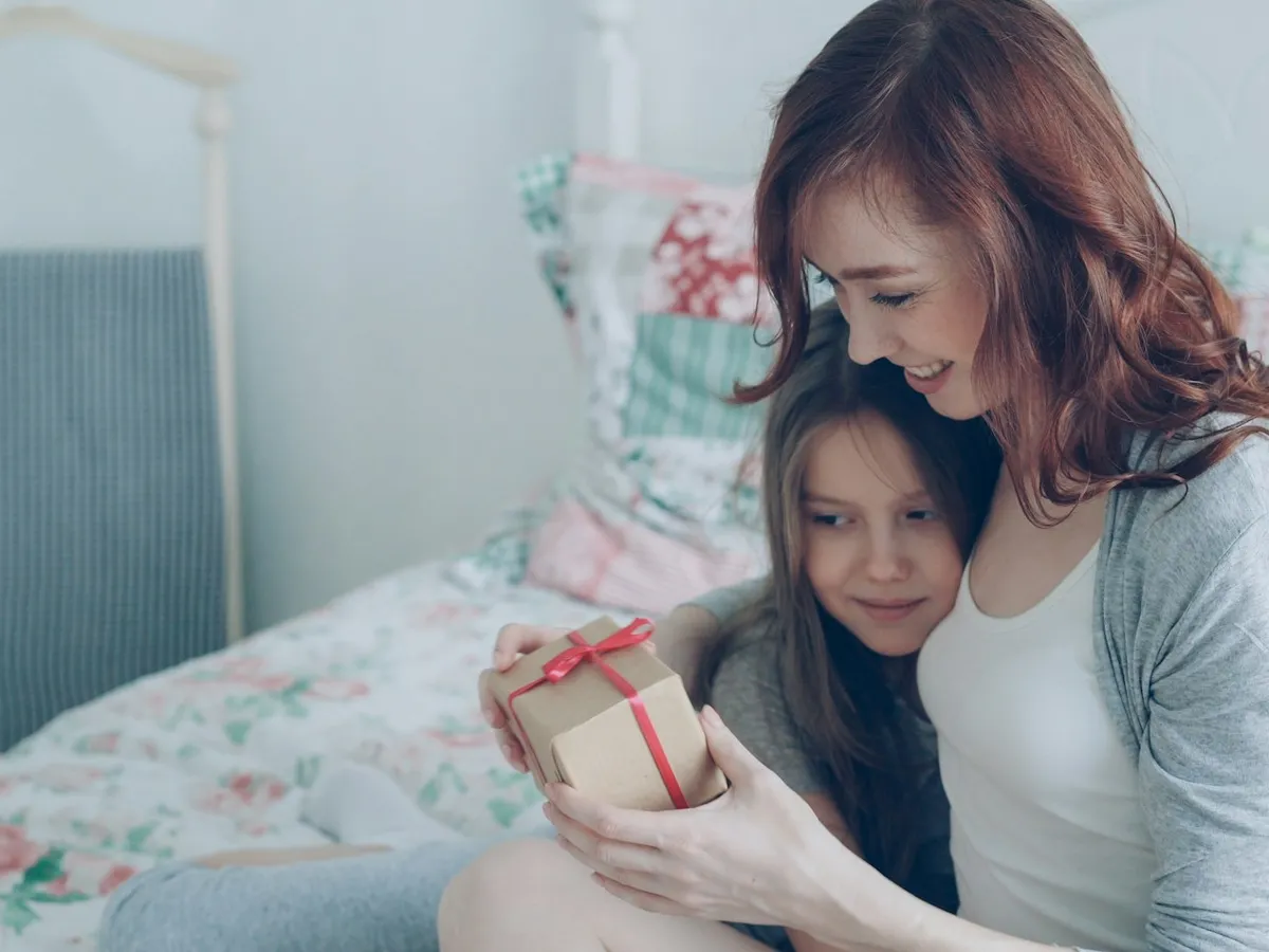 A mother and her little daughter cuddling on a bed with a flowered blanket