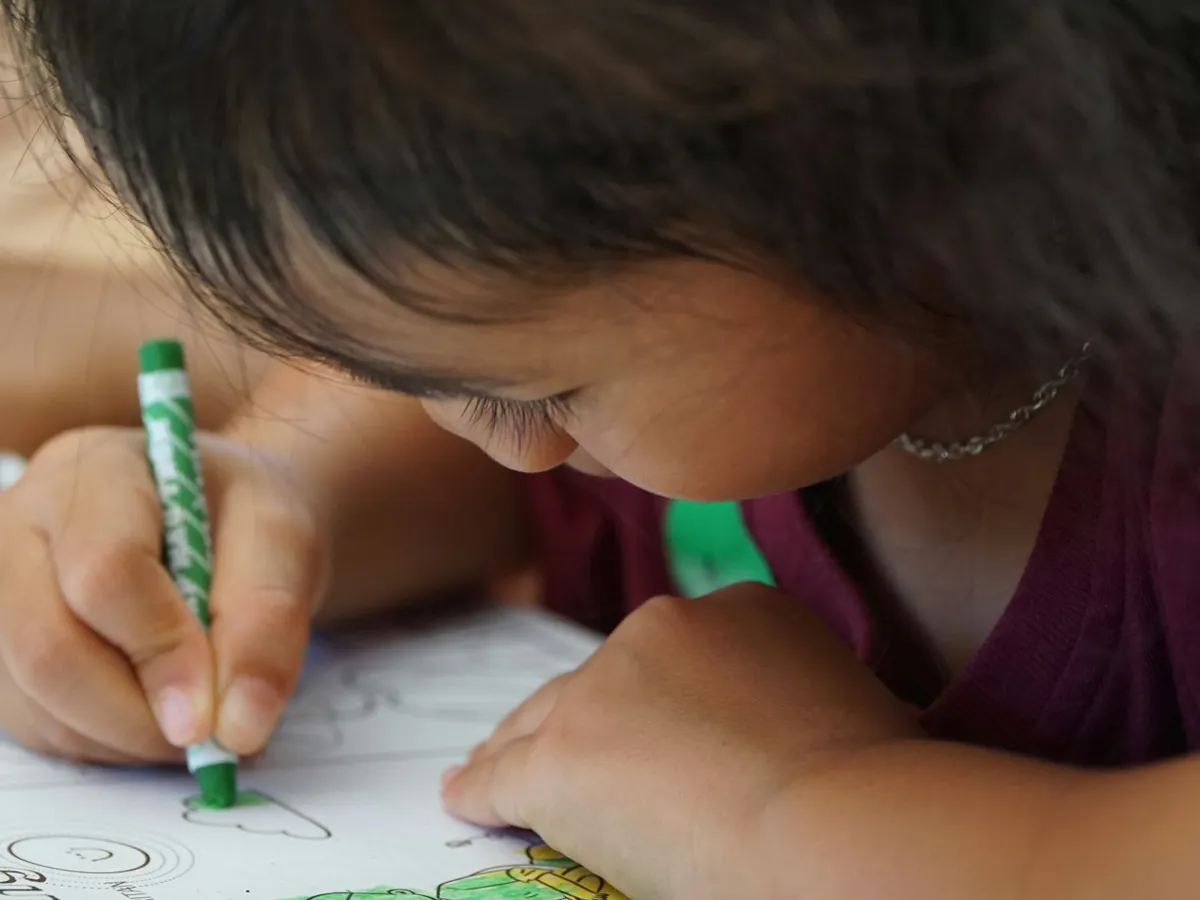 A preschool girl leaning in close and coloring carefully with a green crayon