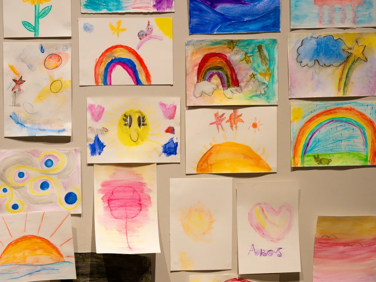 A wall covered with children’s rainbow and sun drawings, displayed proudly