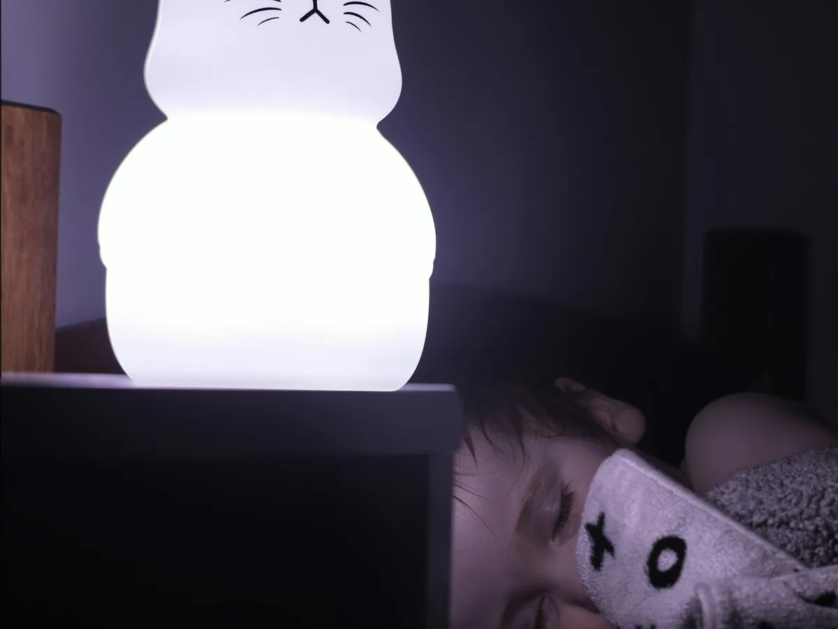 A glowing cat-shaped night light on a bedside table in a dark kids room